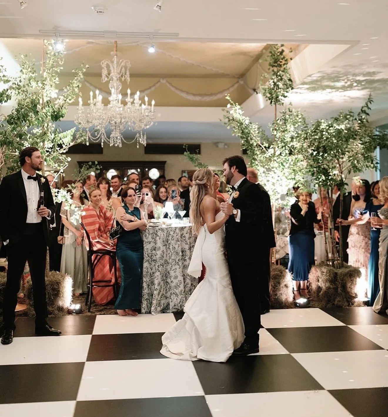 Couple dancing on a checkerboard dance floor beneath a greenery arch and chandelier at a Tulsa reception